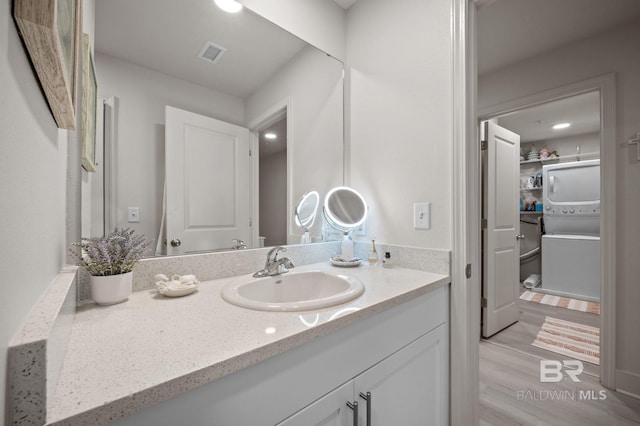 bathroom featuring stacked washing maching and dryer, visible vents, wood finished floors, and vanity