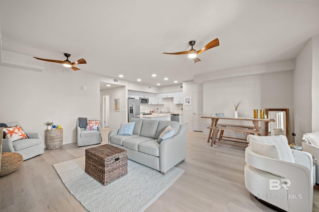 living room with light wood-type flooring, ceiling fan, visible vents, and recessed lighting