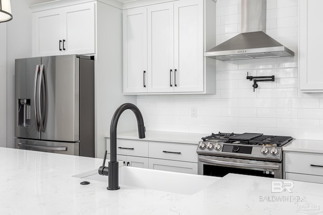 kitchen featuring wall chimney exhaust hood, appliances with stainless steel finishes, backsplash, and white cabinetry