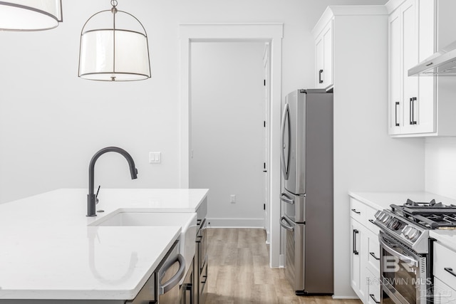 kitchen featuring white cabinets, wall chimney exhaust hood, decorative light fixtures, stainless steel appliances, and light wood-type flooring