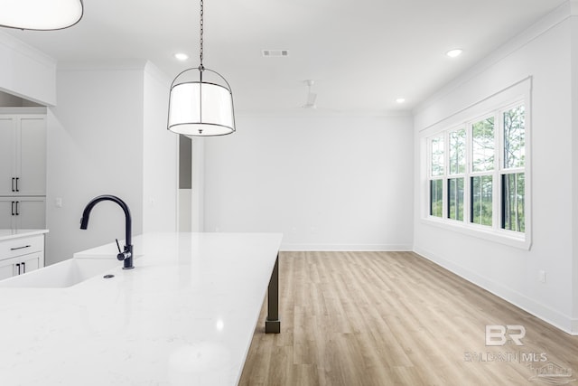 kitchen with visible vents, crown molding, light wood-style floors, white cabinetry, and a sink