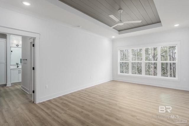 empty room featuring ornamental molding, a raised ceiling, and baseboards