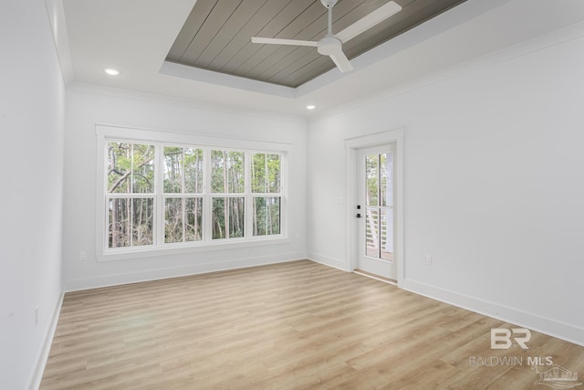 empty room featuring light wood-type flooring, a tray ceiling, ornamental molding, and baseboards