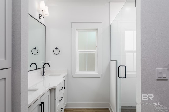 full bath with double vanity, a stall shower, a sink, wood finished floors, and baseboards