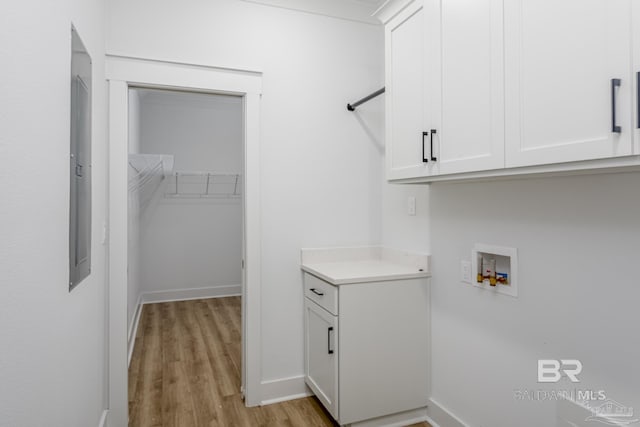 clothes washing area featuring light wood-style flooring, washer hookup, cabinet space, and baseboards