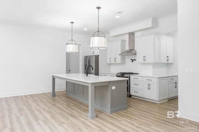 kitchen featuring an island with sink, wall chimney exhaust hood, light wood-style flooring, stainless steel appliances, and light countertops