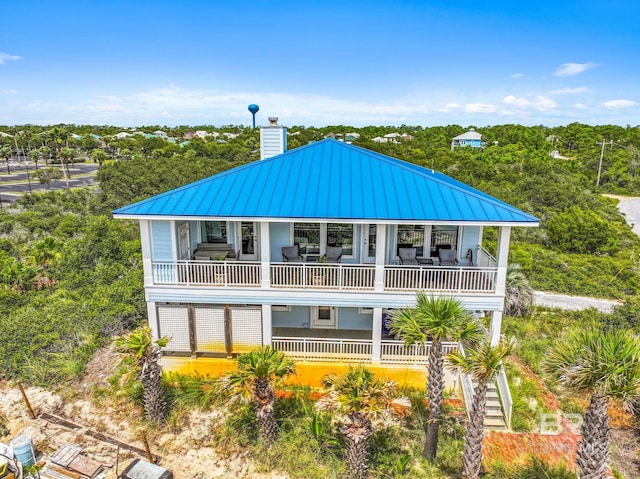 back of house with a standing seam roof, a balcony, metal roof, and a chimney