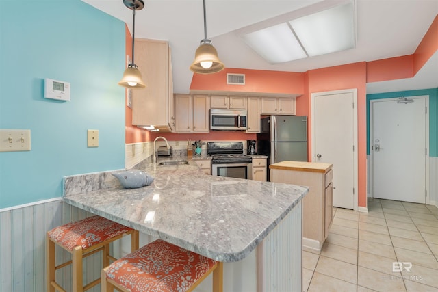 kitchen with sink, light tile floors, hanging light fixtures, a breakfast bar, and stainless steel appliances
