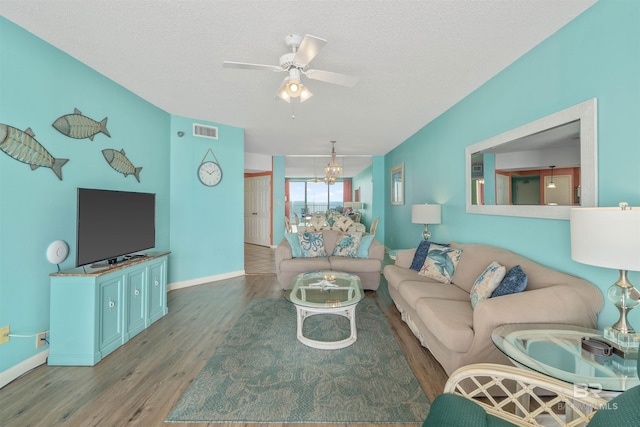 living room featuring a textured ceiling, ceiling fan with notable chandelier, and dark wood-type flooring