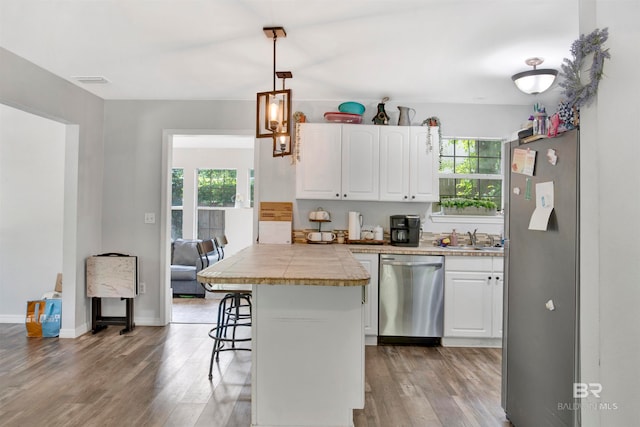 kitchen featuring plenty of natural light, stainless steel appliances, hardwood / wood-style flooring, a kitchen bar, and white cabinetry