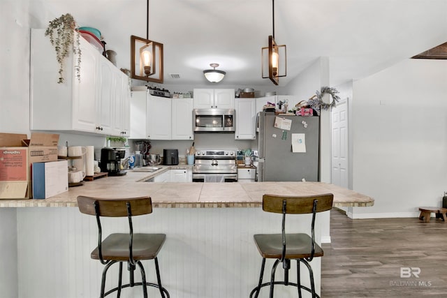 kitchen featuring decorative light fixtures, kitchen peninsula, stainless steel appliances, hardwood / wood-style flooring, and white cabinetry