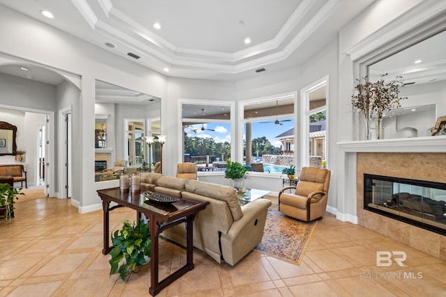 living room with a tray ceiling, a tile fireplace, crown molding, and light tile patterned flooring