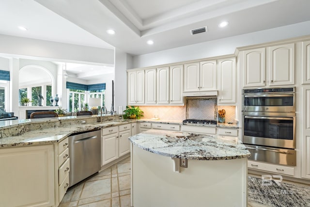 kitchen featuring tasteful backsplash, a kitchen island, sink, light stone countertops, and appliances with stainless steel finishes