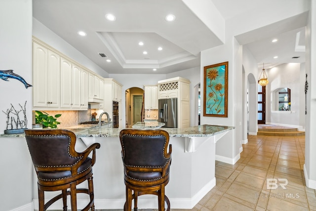 kitchen with a kitchen breakfast bar, kitchen peninsula, light stone countertops, decorative backsplash, and stainless steel fridge with ice dispenser