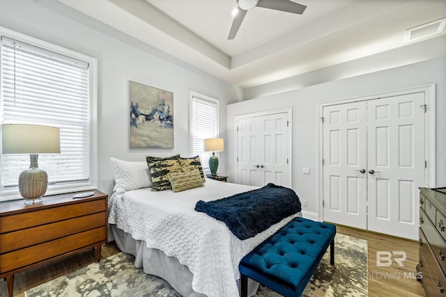 bedroom with ceiling fan, hardwood / wood-style flooring, and multiple closets