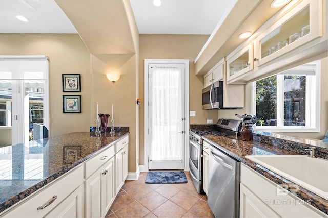 kitchen featuring stainless steel appliances, sink, white cabinetry, dark stone countertops, and light tile patterned flooring