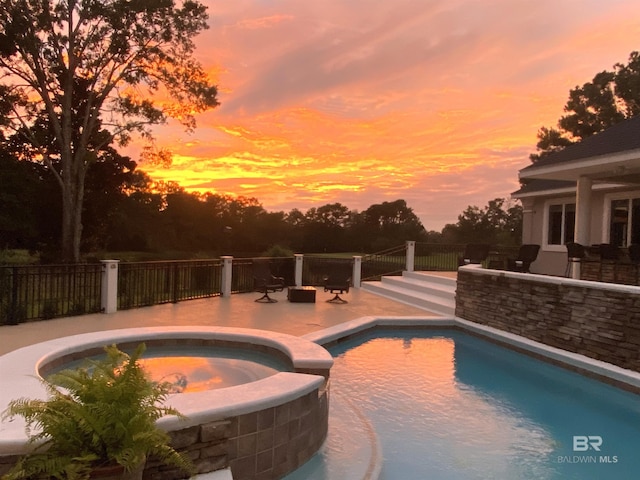 pool at dusk featuring a patio area and an in ground hot tub