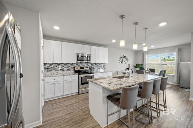 kitchen featuring pendant lighting, a kitchen island with sink, appliances with stainless steel finishes, and white cabinetry