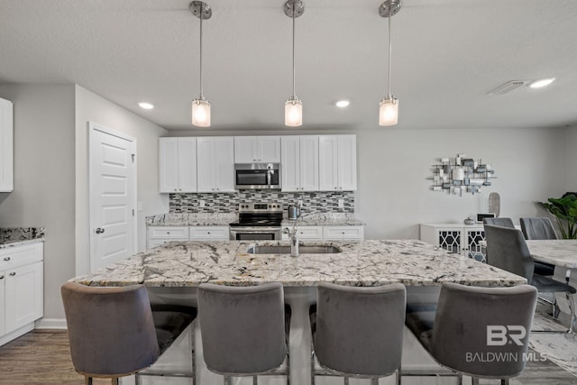 kitchen featuring a center island with sink, appliances with stainless steel finishes, hanging light fixtures, and tasteful backsplash