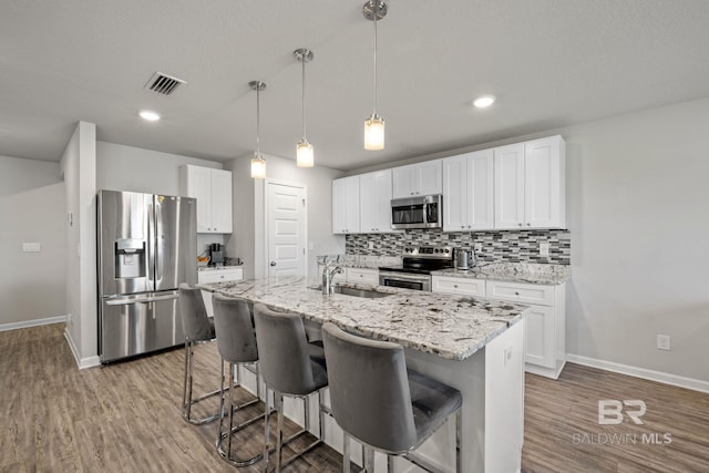 kitchen with an island with sink, stainless steel appliances, white cabinetry, and sink