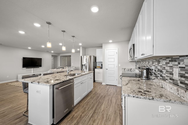 kitchen featuring wood-type flooring, sink, white cabinetry, stainless steel appliances, and a center island with sink