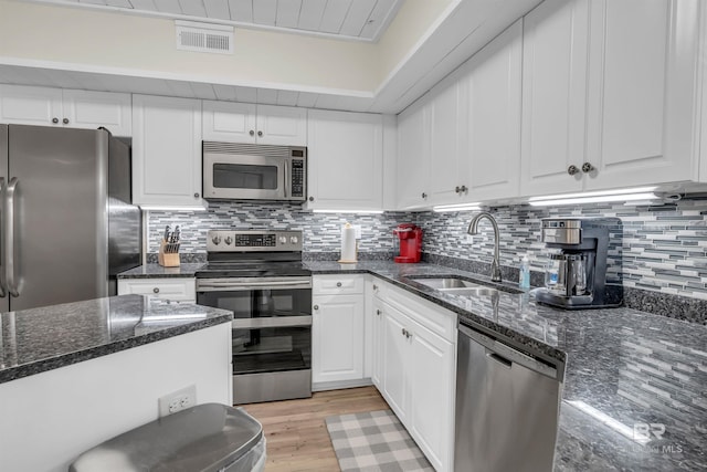 kitchen with stainless steel appliances, white cabinetry, dark stone countertops, and sink