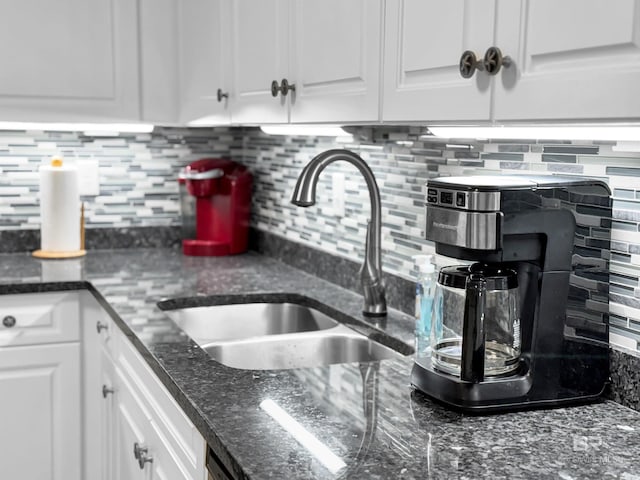 kitchen with tasteful backsplash, white cabinetry, dark stone countertops, and sink