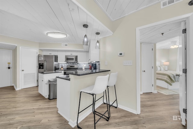 kitchen with white cabinetry, stainless steel appliances, tasteful backsplash, kitchen peninsula, and decorative light fixtures