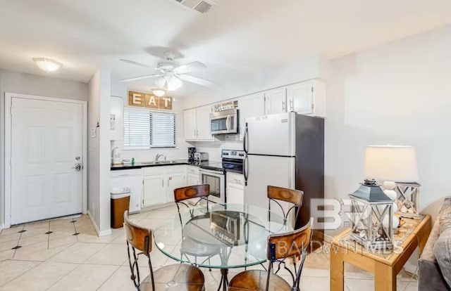 kitchen with appliances with stainless steel finishes, ceiling fan, white cabinets, sink, and light tile flooring