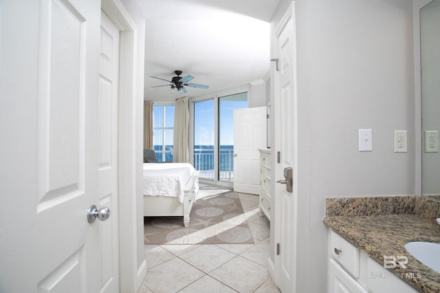 interior space featuring tile patterned floors, vanity, ceiling fan, a water view, and a wall of windows