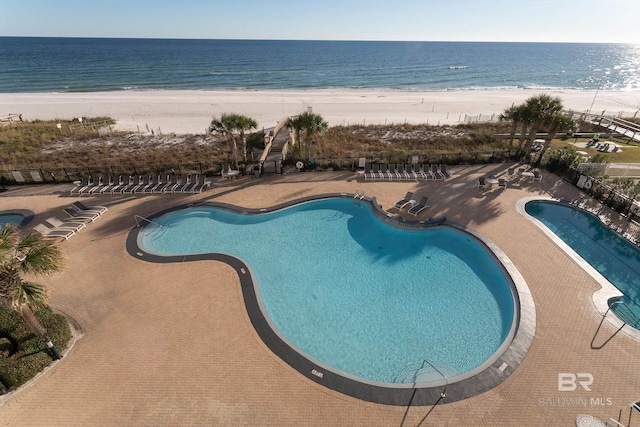 view of swimming pool with a view of the beach, a water view, and a patio area