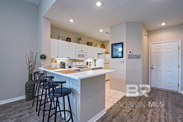 kitchen featuring a peninsula, white appliances, baseboards, white cabinets, and a kitchen bar