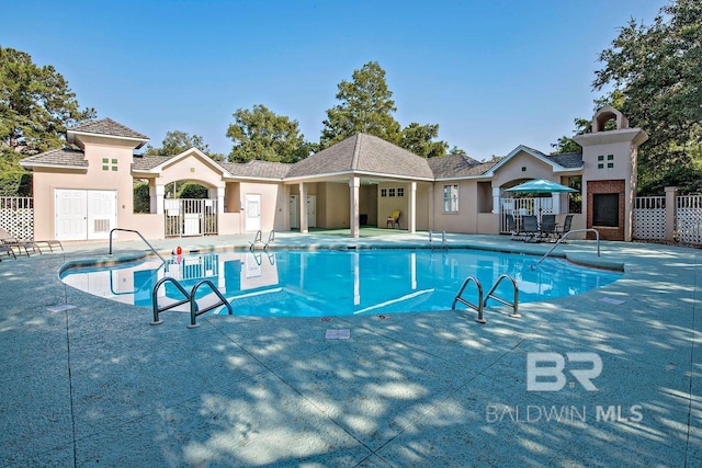 community pool featuring fence, exterior fireplace, and a patio