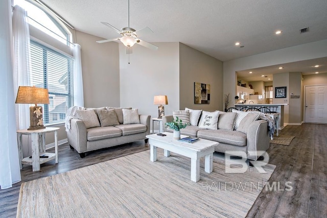 living room featuring a textured ceiling, dark wood-type flooring, visible vents, and baseboards