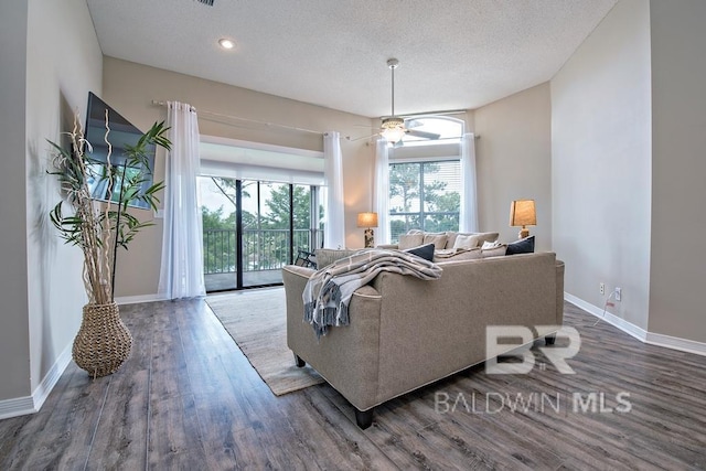 living room with ceiling fan, a textured ceiling, baseboards, and wood finished floors