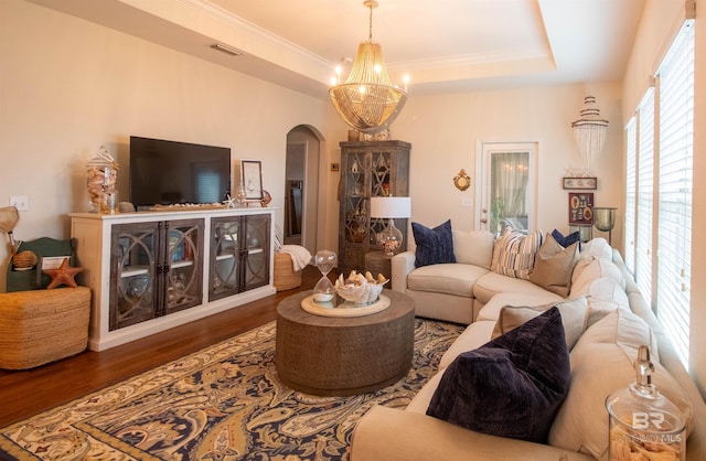 living area with crown molding, a raised ceiling, visible vents, arched walkways, and wood finished floors