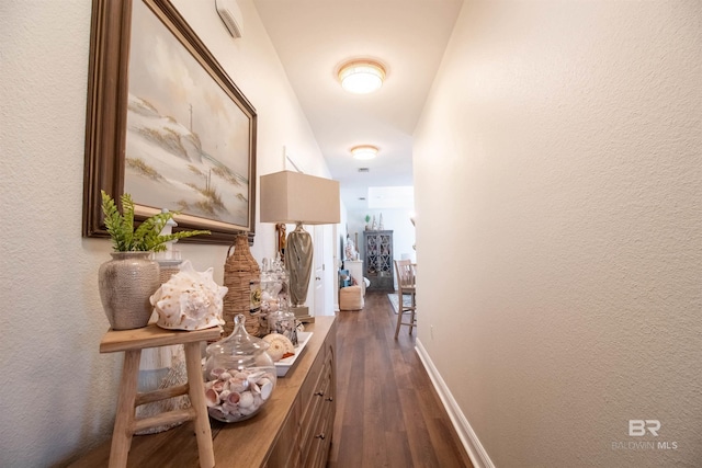 hall featuring baseboards, a textured wall, and dark wood finished floors