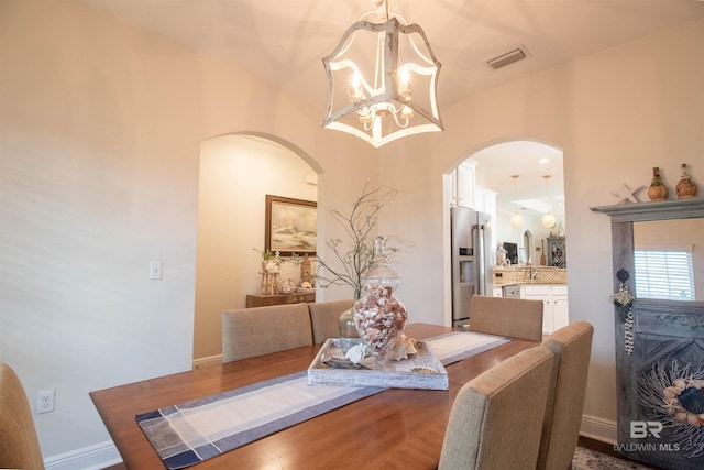 dining area featuring dark wood-style flooring, a chandelier, visible vents, baseboards, and arched walkways
