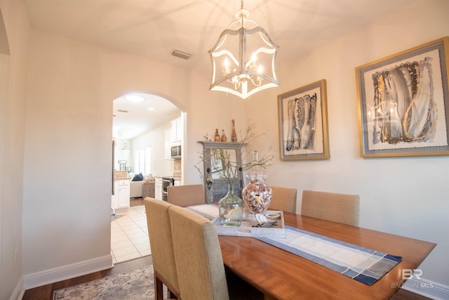 dining area with a notable chandelier, visible vents, baseboards, arched walkways, and wood finished floors
