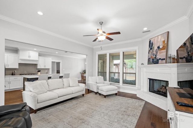 living room with ceiling fan, ornamental molding, wood-type flooring, and a fireplace