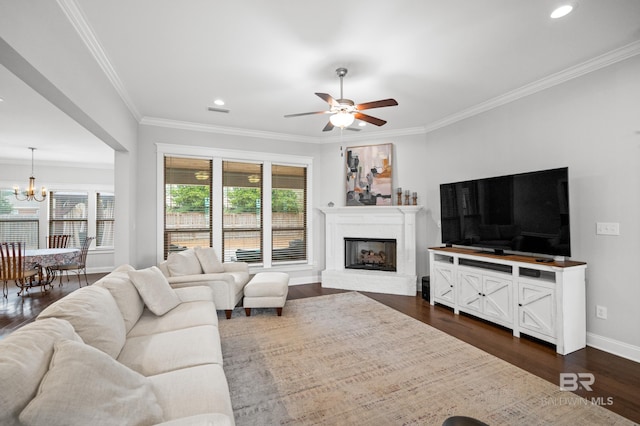 living room with dark wood-type flooring, crown molding, ceiling fan with notable chandelier, and a brick fireplace