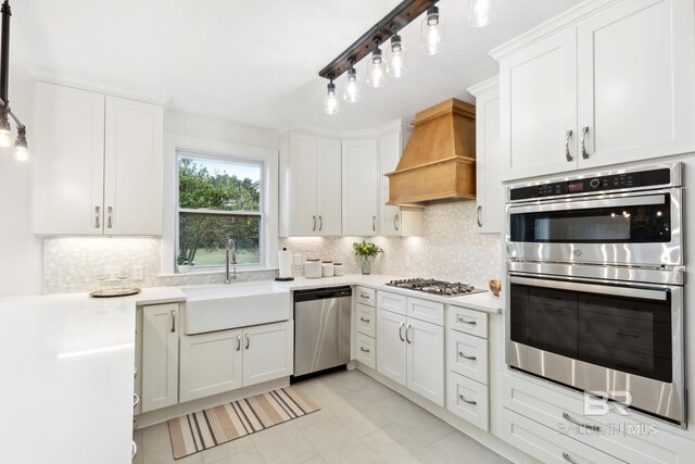 kitchen featuring appliances with stainless steel finishes, premium range hood, white cabinetry, and sink