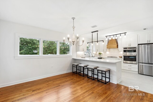 kitchen featuring appliances with stainless steel finishes, white cabinets, kitchen peninsula, custom exhaust hood, and light hardwood / wood-style flooring