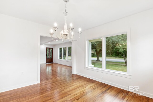 empty room with a notable chandelier and light hardwood / wood-style floors