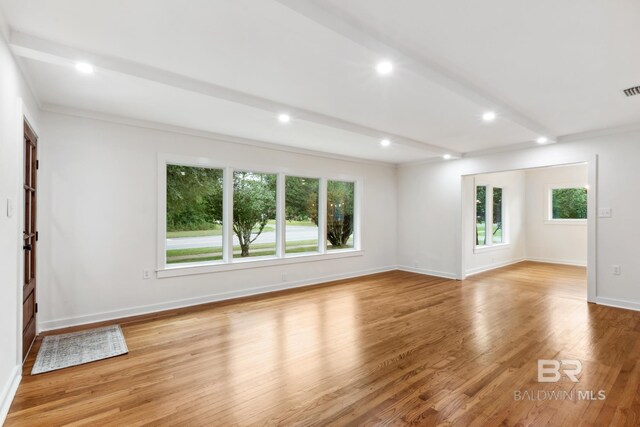 empty room with a healthy amount of sunlight, light hardwood / wood-style floors, crown molding, and beamed ceiling