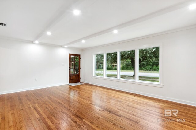 spare room featuring light hardwood / wood-style floors, ornamental molding, and beamed ceiling