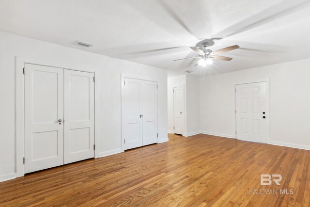 unfurnished bedroom featuring ceiling fan, multiple closets, and light hardwood / wood-style flooring