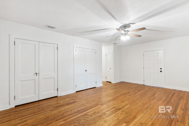 unfurnished bedroom featuring baseboards, visible vents, two closets, and light wood-style floors