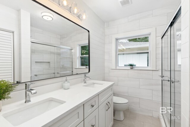 bathroom with tile walls, tile patterned floors, a shower with shower door, vanity, and toilet