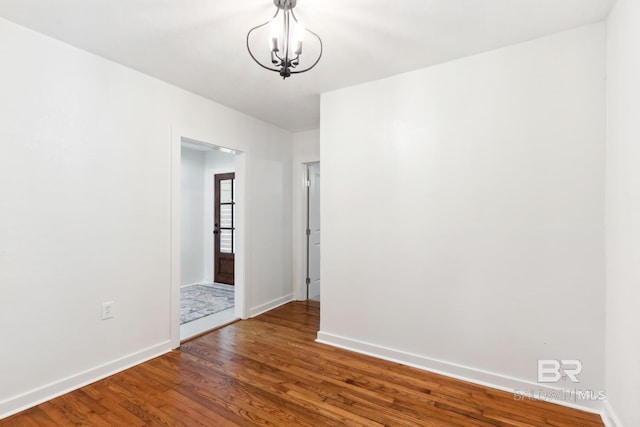 unfurnished room featuring baseboards, wood finished floors, and a chandelier
